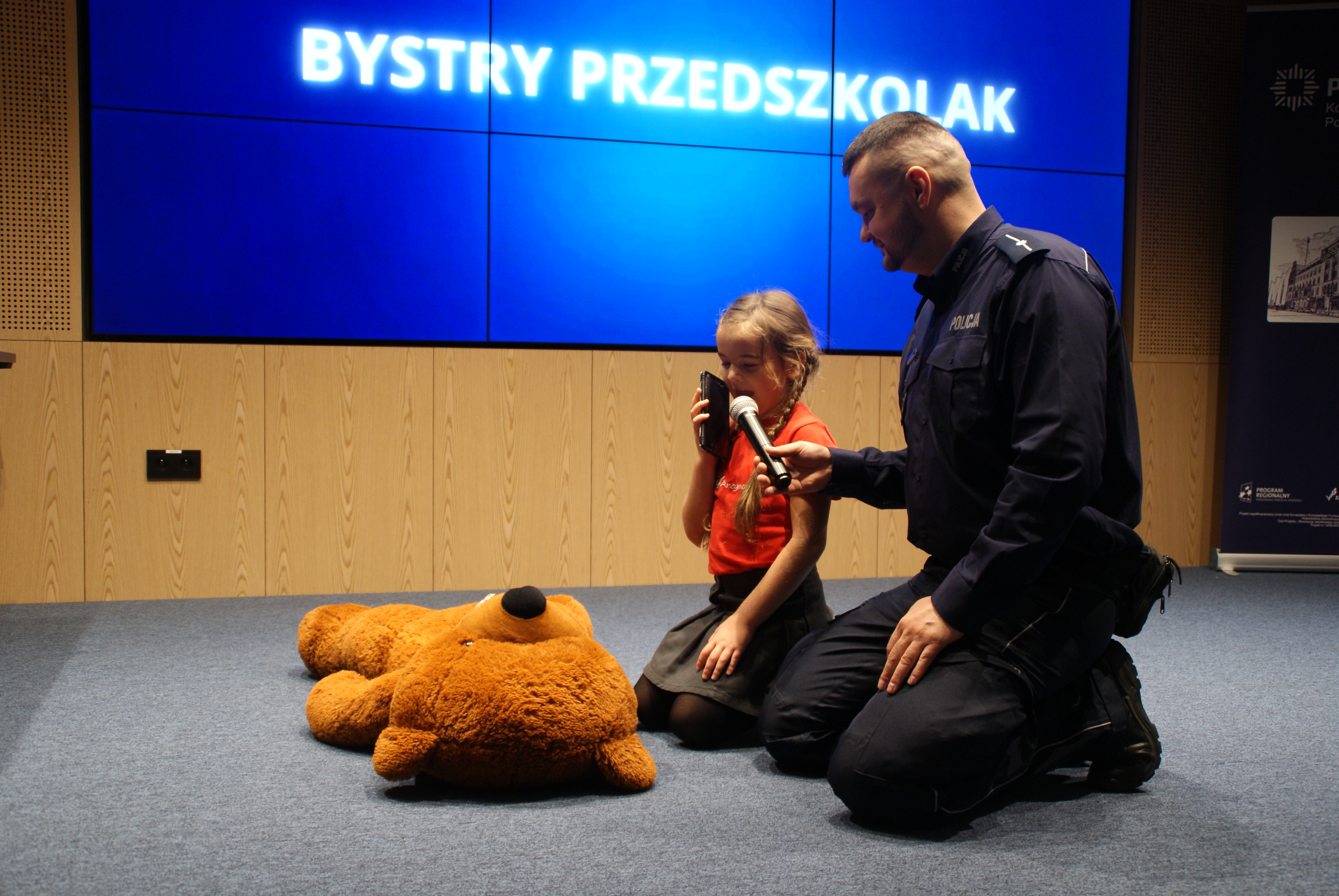 Udzielanie pierwszej pomocy pluszowemu pacjentowi Uczestniczka klęczy przy pluszowym misiu, odgrywającym rolę pacjenta