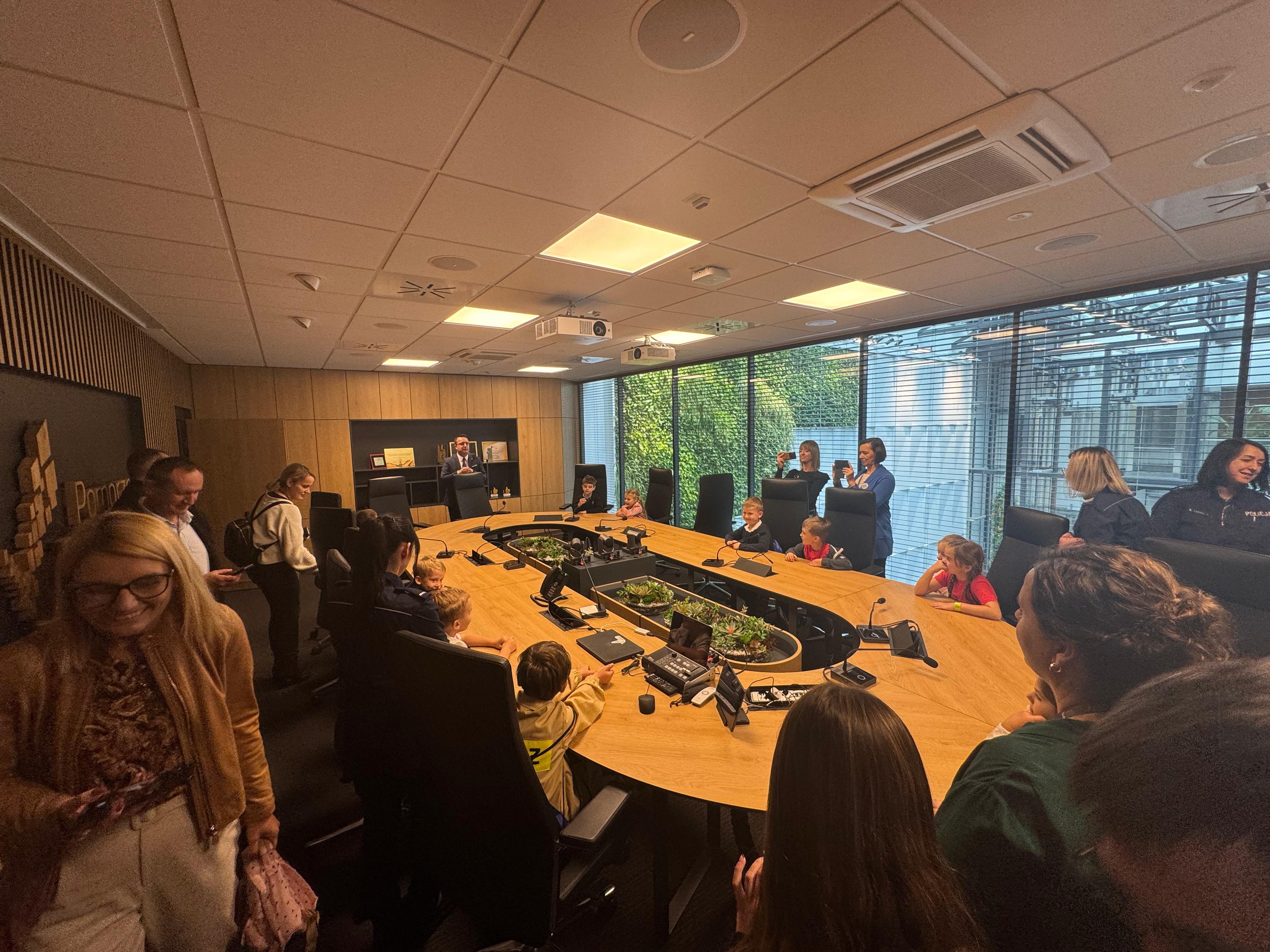 Z wizytą w sali posiedzeń Zarządu Województwa Dzieci siedzące wokół stołu w otoczeniu opiekunów.