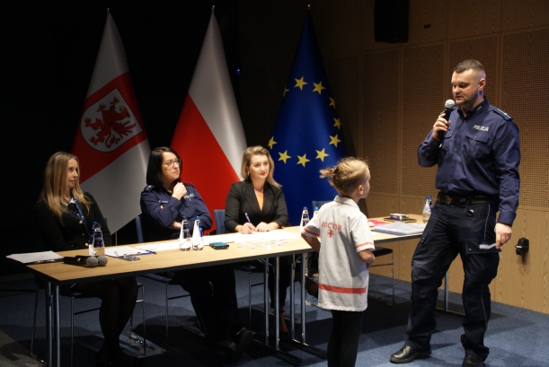 Prowadzący policjant i uczestnik stoją przed stołem sędziowskim