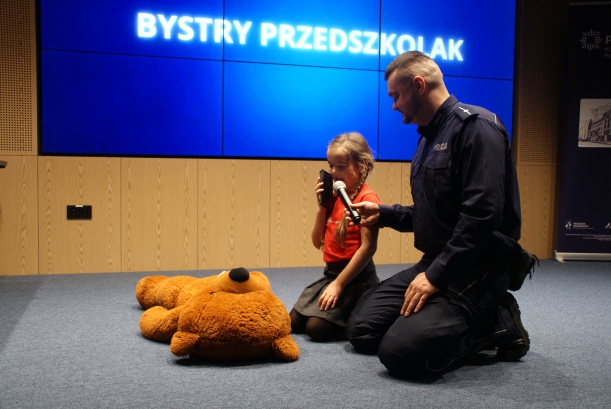 Uczestniczka klęczy przy pluszowym misiu, odgrywającym rolę pacjenta