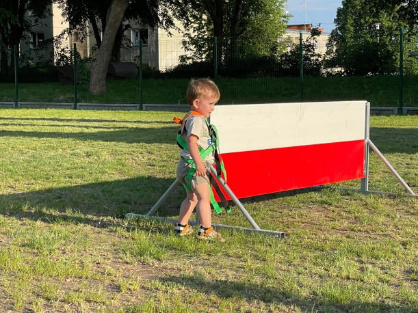 Dziecko w uprzęży alpinistycznej na tle elementu toru przeszkód