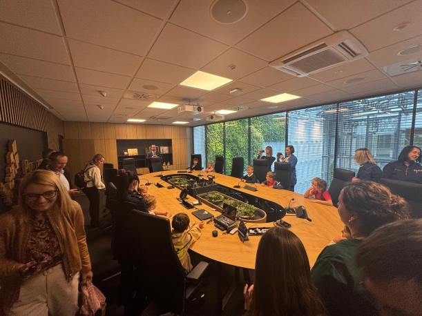 Dzieci siedzące wokół stołu w otoczeniu opiekunów.