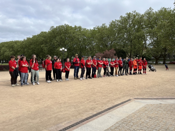 Zdjęcie zbiorowe - sześć zespołów ratowniczych ustawionych w szyku, w tle Pomnik Czynu Polaków